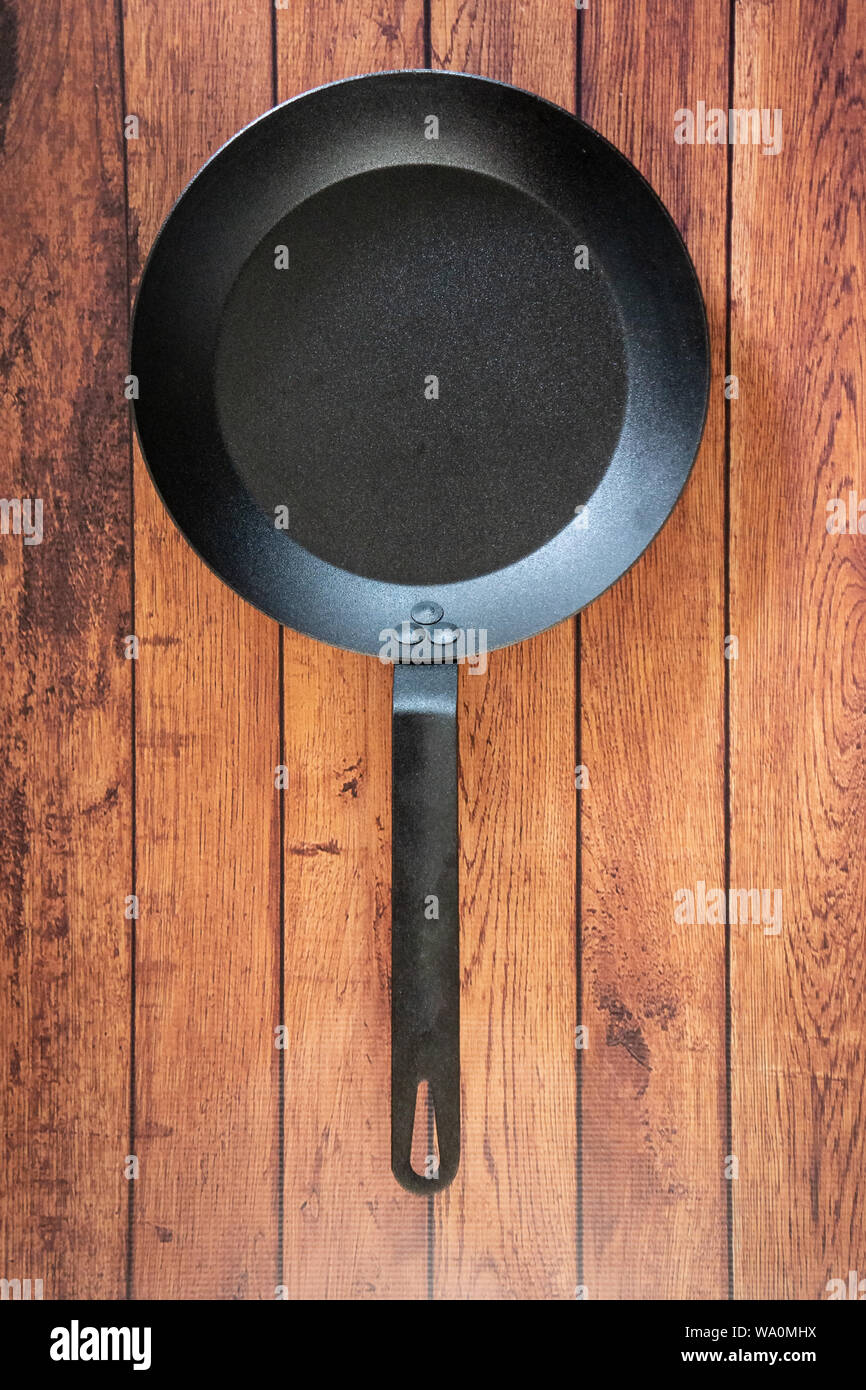 Isolare in acciaio al carbonio skillet pan su un sfondo di legno - tetto vista dall'alto del piatto concetto laici. Professional grade pentole arnese apparecchiature utilizzate in Foto Stock