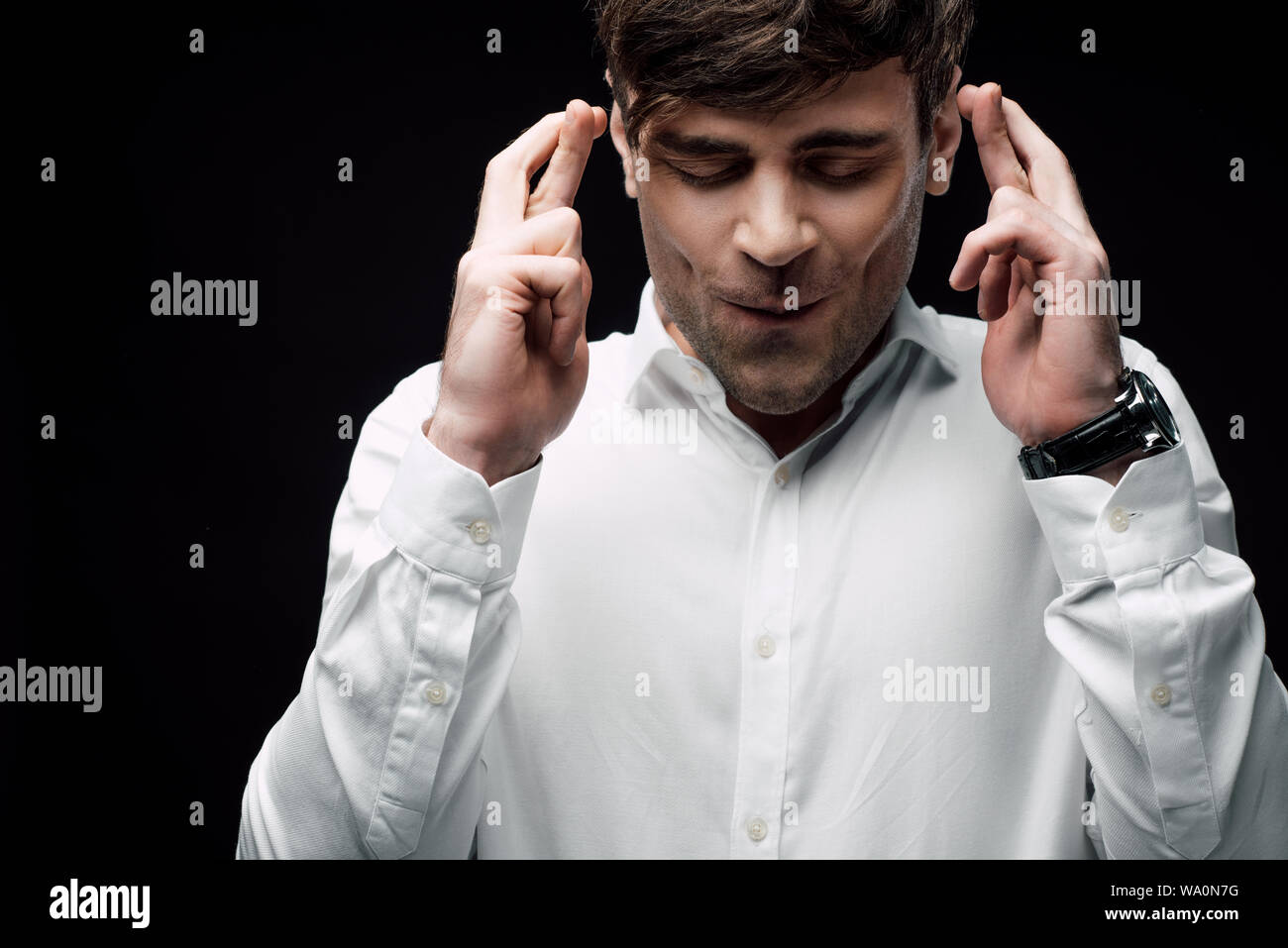 Imprenditore con gli occhi chiusi tenendo le dita incrociate isolato sul nero, emozione umana e il concetto di espressione Foto Stock