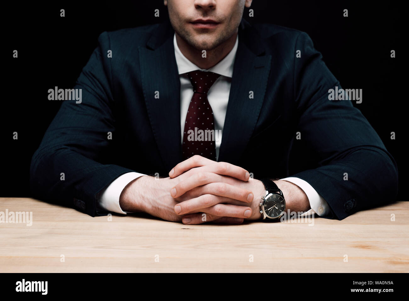 Vista parziale di imprenditore seduta a tavola con le mani chiuse isolate su nero, emozione umana e il concetto di espressione Foto Stock