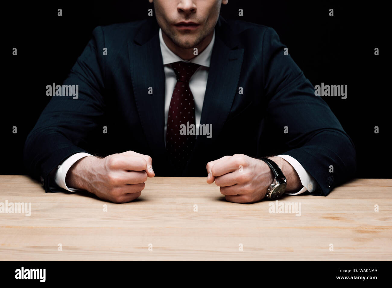 Vista parziale di angry businessman seduta a tavola e tenendo i pugni isolato sul nero, emozione umana e il concetto di espressione Foto Stock