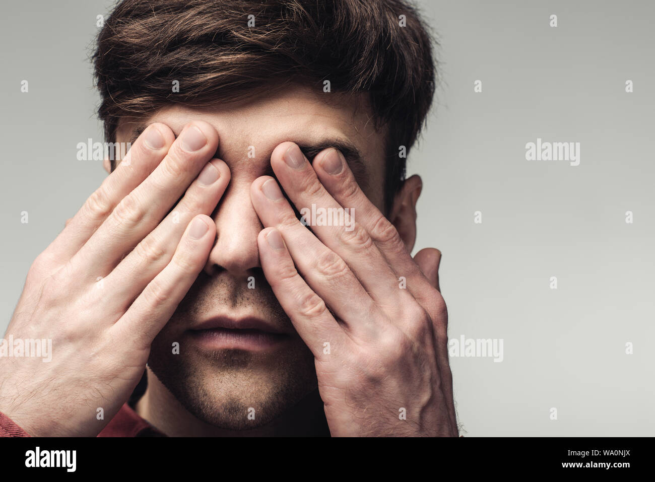 Cieco che copre gli occhi con le mani isolate su grigio, emozioni umane e concetto di espressione Foto Stock