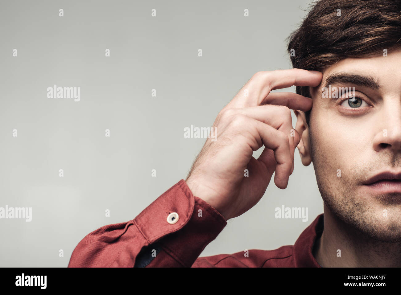 Ritagliato colpo di pensieroso uomo che guarda lontano e toccando la testa isolata sul grigio, emozioni umane e concetto di espressione Foto Stock