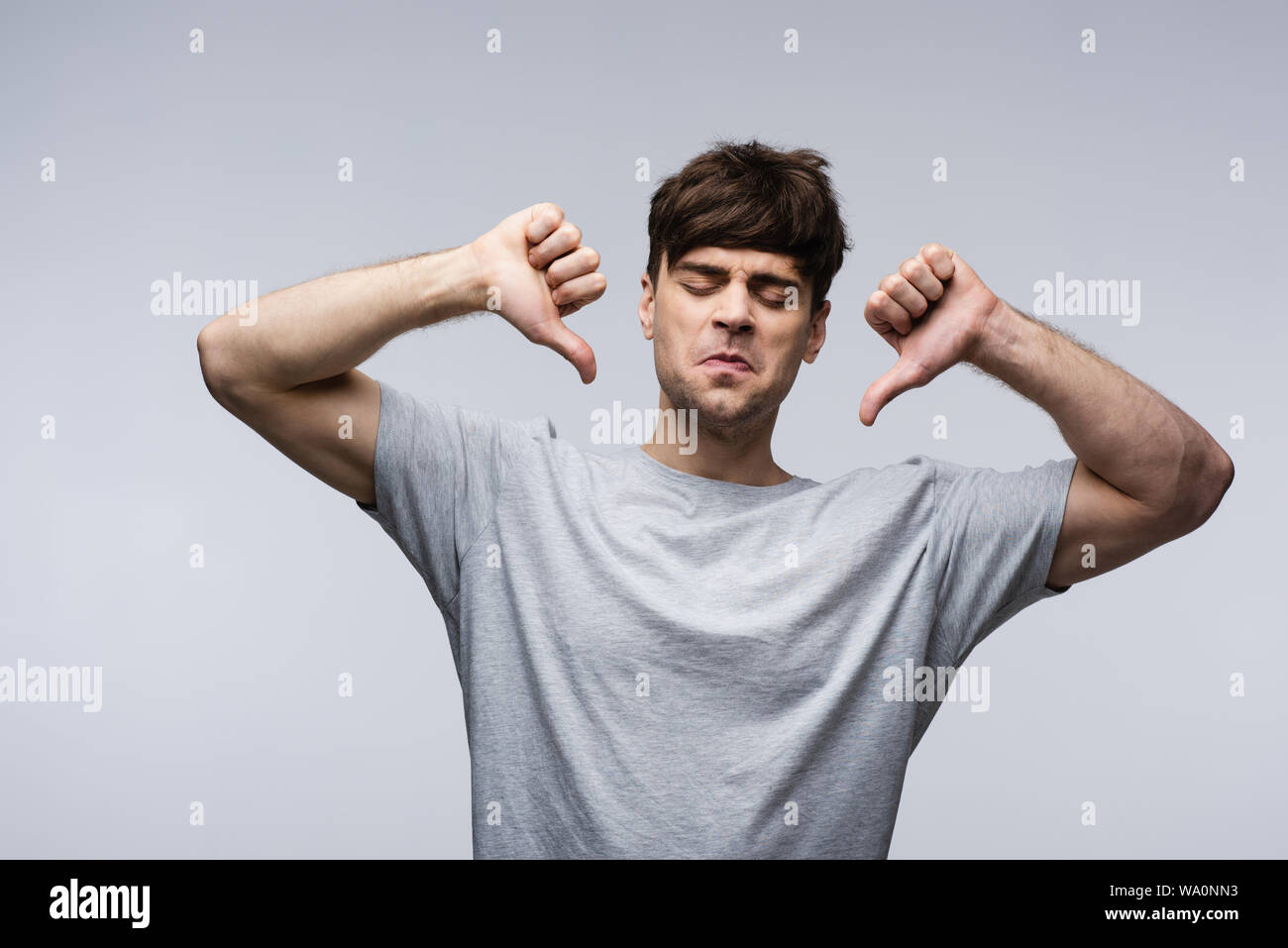 Dispiacque all uomo che mostra il pollice verso il basso sulla isolato grigio, emozioni umane e concetto di espressione Foto Stock