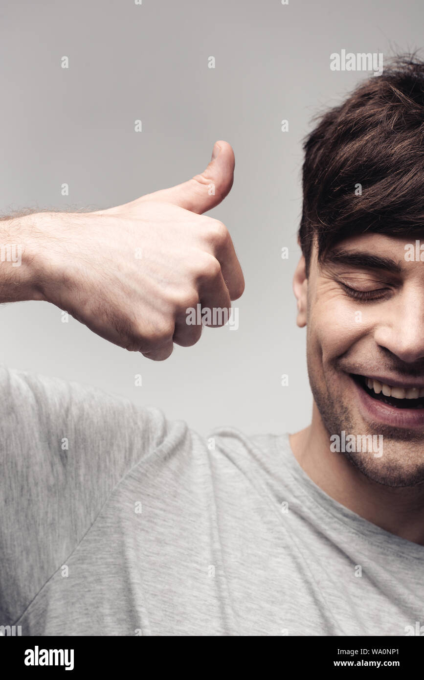 Allegro uomo mostra pollice in alto isolato su grigio, emozione umana e il concetto di espressione Foto Stock