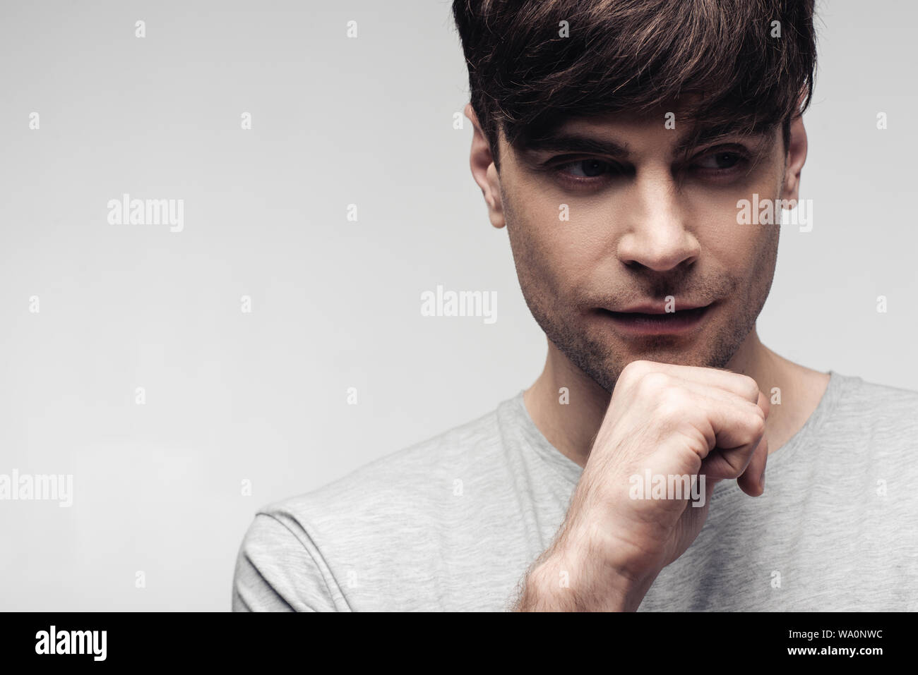 Bel uomo sognante guardando lontano tenendo la mano vicino alla faccia isolati su grigio, emozioni umane e concetto di espressione Foto Stock
