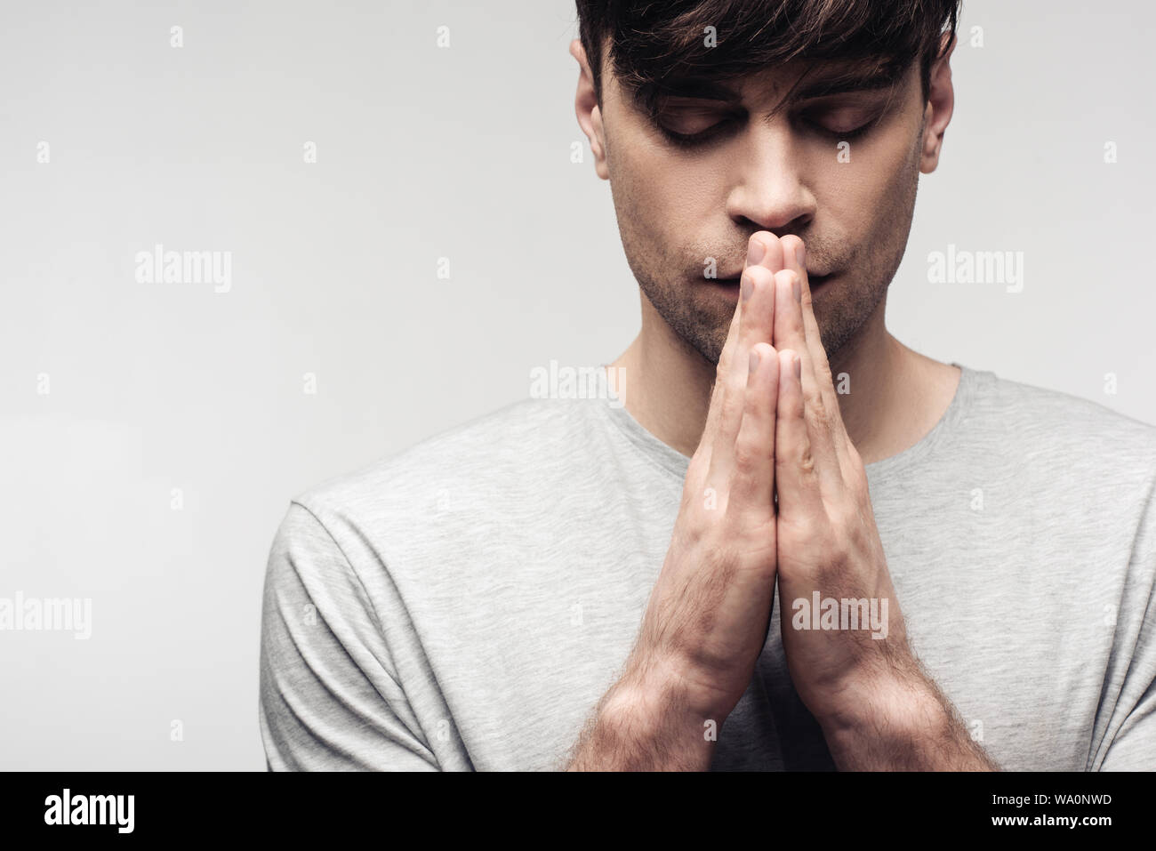 Uomo serio con gli occhi chiusi che mostra pregando gesto isolato sul grigio, emozioni umane e concetto di espressione Foto Stock