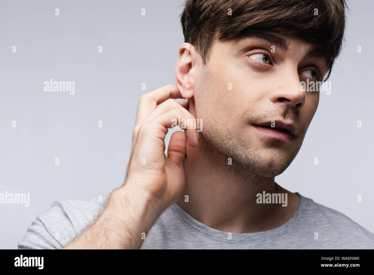 Malinconici l uomo che guarda lontano e toccando il collo isolati su grigio, emozioni umane e concetto di espressione Foto Stock