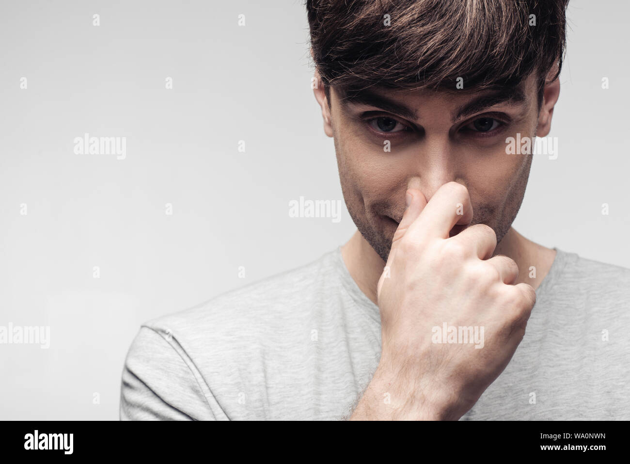 Sorridente uomo sognante toccando il naso isolati su grigio, emozioni umane e concetto di espressione Foto Stock
