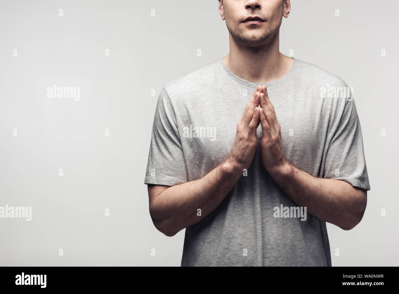 Vista ritagliata dell uomo che mostra pregando gesto isolato sul grigio, emozioni umane e concetto di espressione Foto Stock