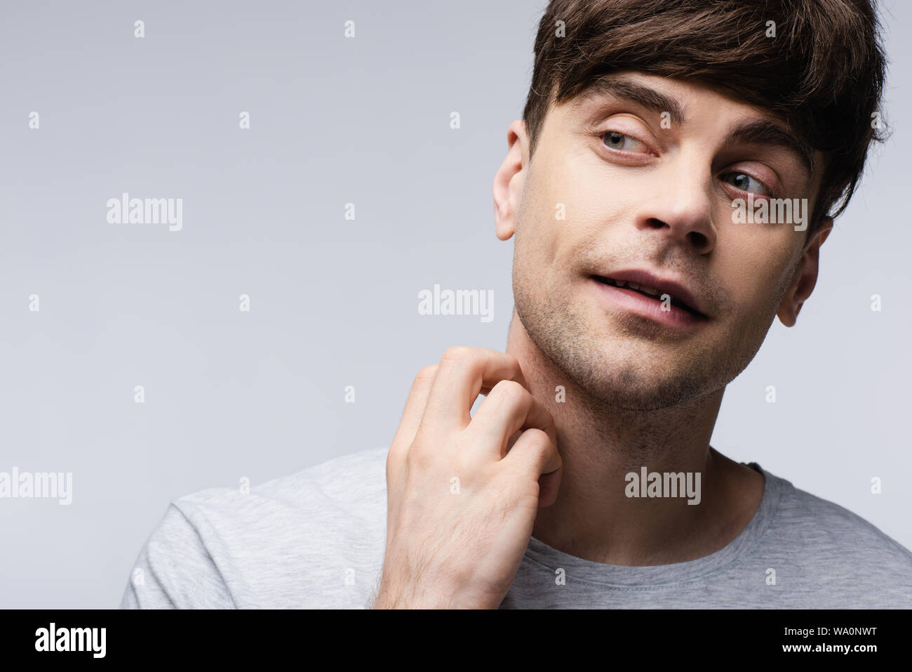 Uomo sorridente che guarda lontano e tenendo la mano vicino al collo isolati su grigio, emozioni umane e concetto di espressione Foto Stock