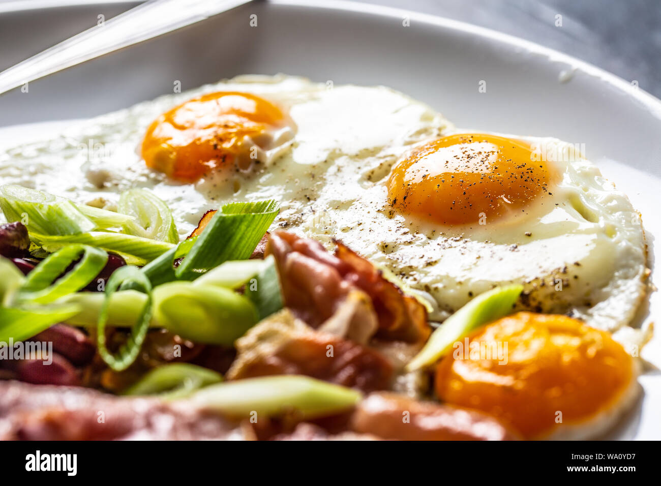 Prima colazione Inglese con uova, pancetta, fagioli e cipolle iyoung nella piastra bianca Foto Stock
