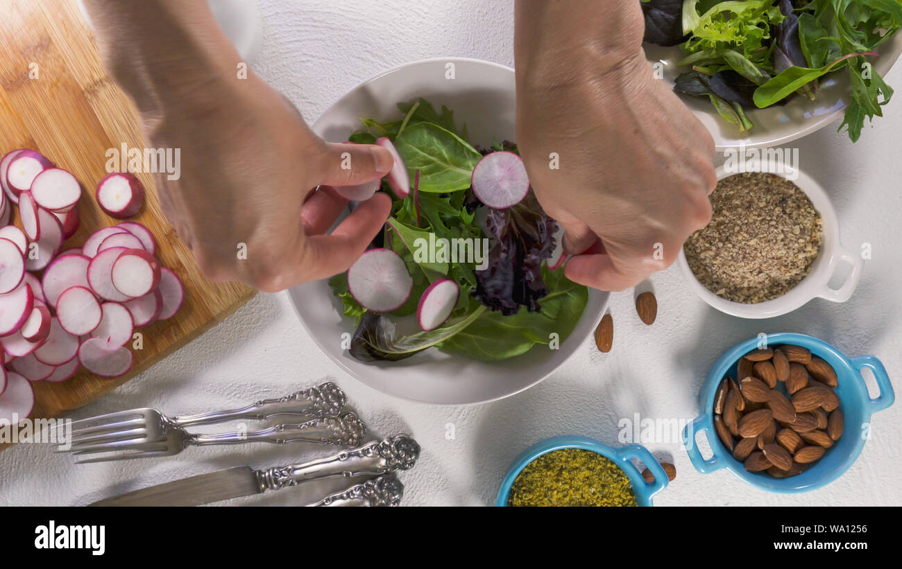 Mix di erbe con insalata fresca di ravanello organico, lattughe e spinaci, alcuni condimento, mandorle e olio vegetale. Close up su sfondo bianco, Donna mani Foto Stock