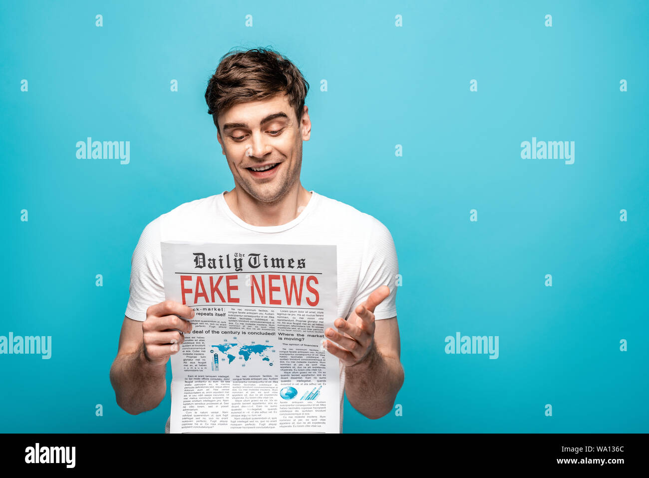 Sorridente giovane quotidiano di lettura con false notizie su sfondo blu Foto Stock