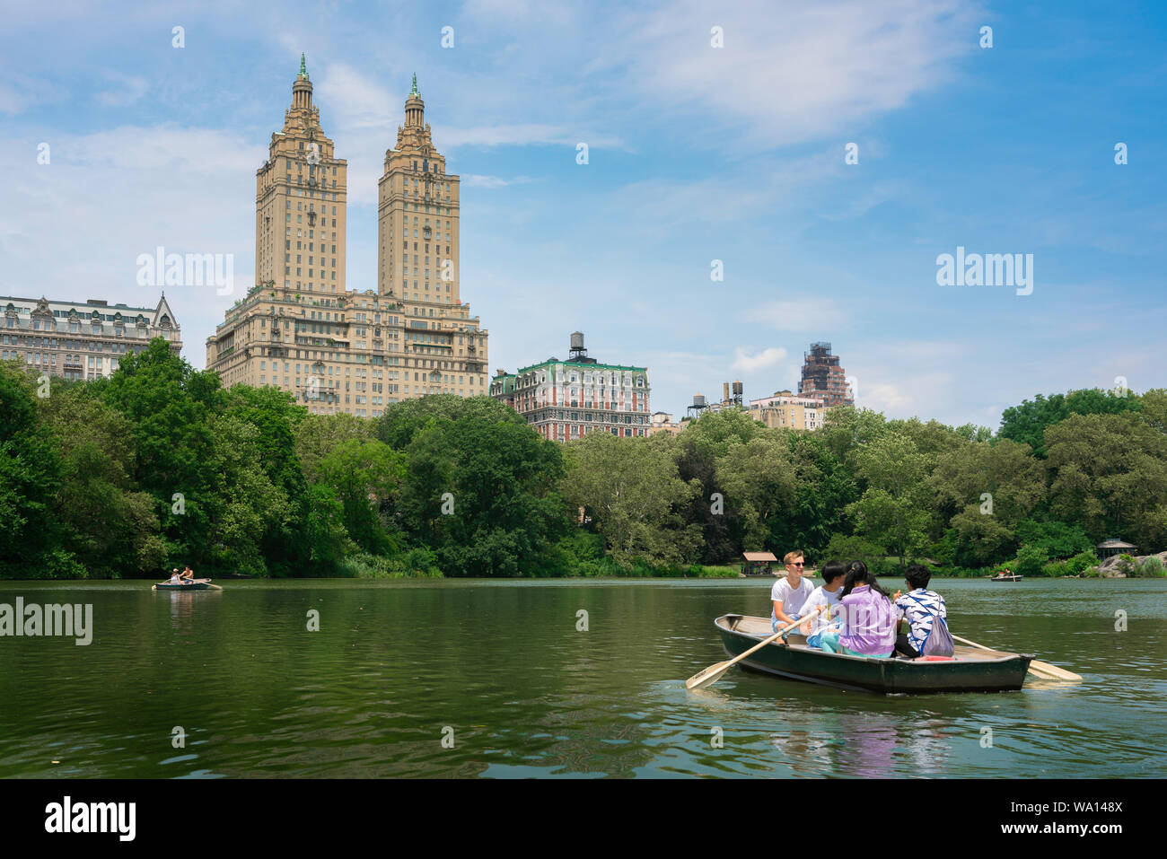 New York Central Park, vista in estate di persone imbarcazioni a remi su Central Park Lake con il San Remo edificio in background, Manhattan NYC, STATI UNITI D'AMERICA Foto Stock
