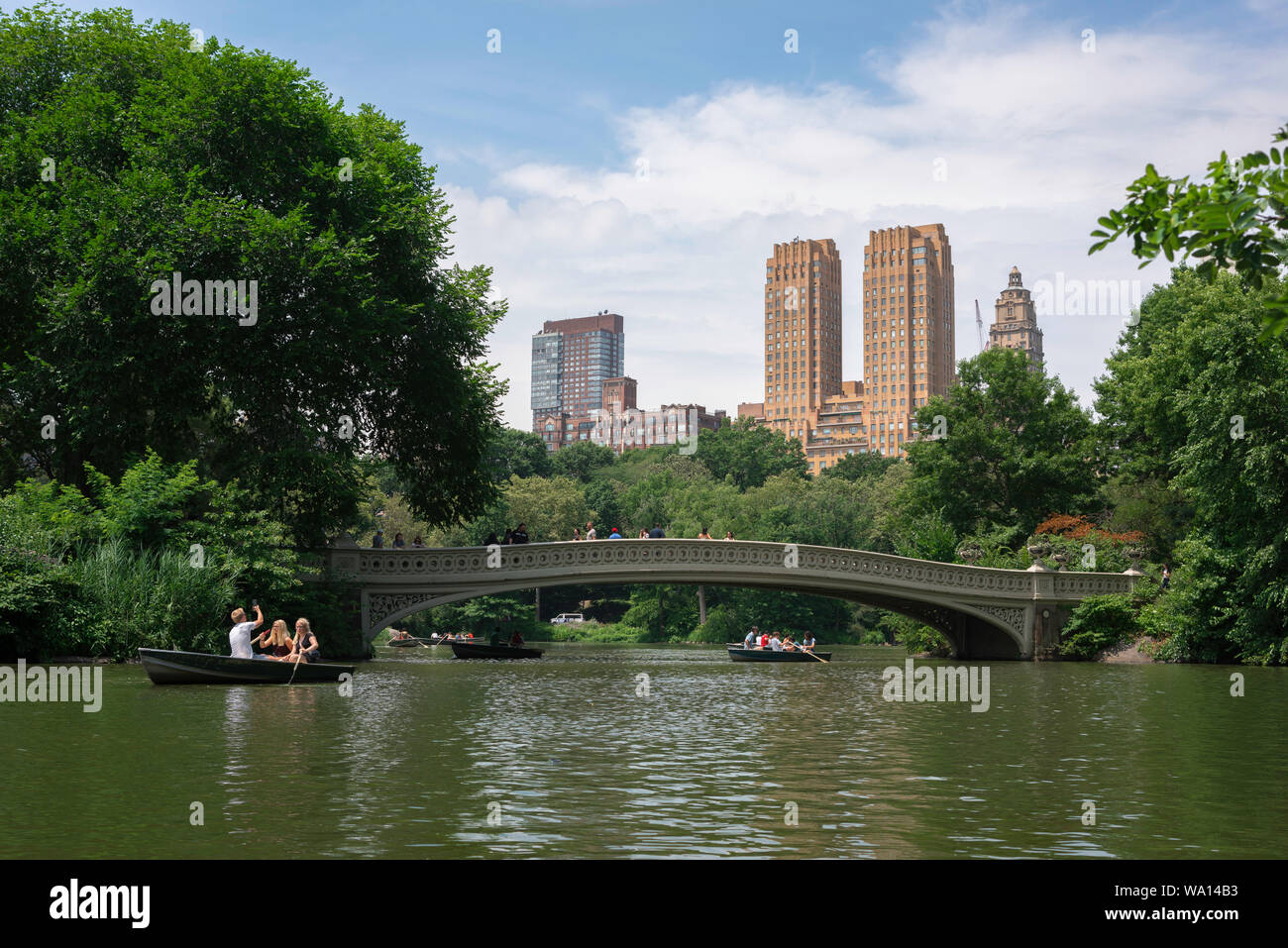 La città di New York, vista in estate di persone imbarcazioni a remi su Central Park Lake con il maestoso edificio di appartamenti in background, Manhattan NYC, STATI UNITI D'AMERICA Foto Stock