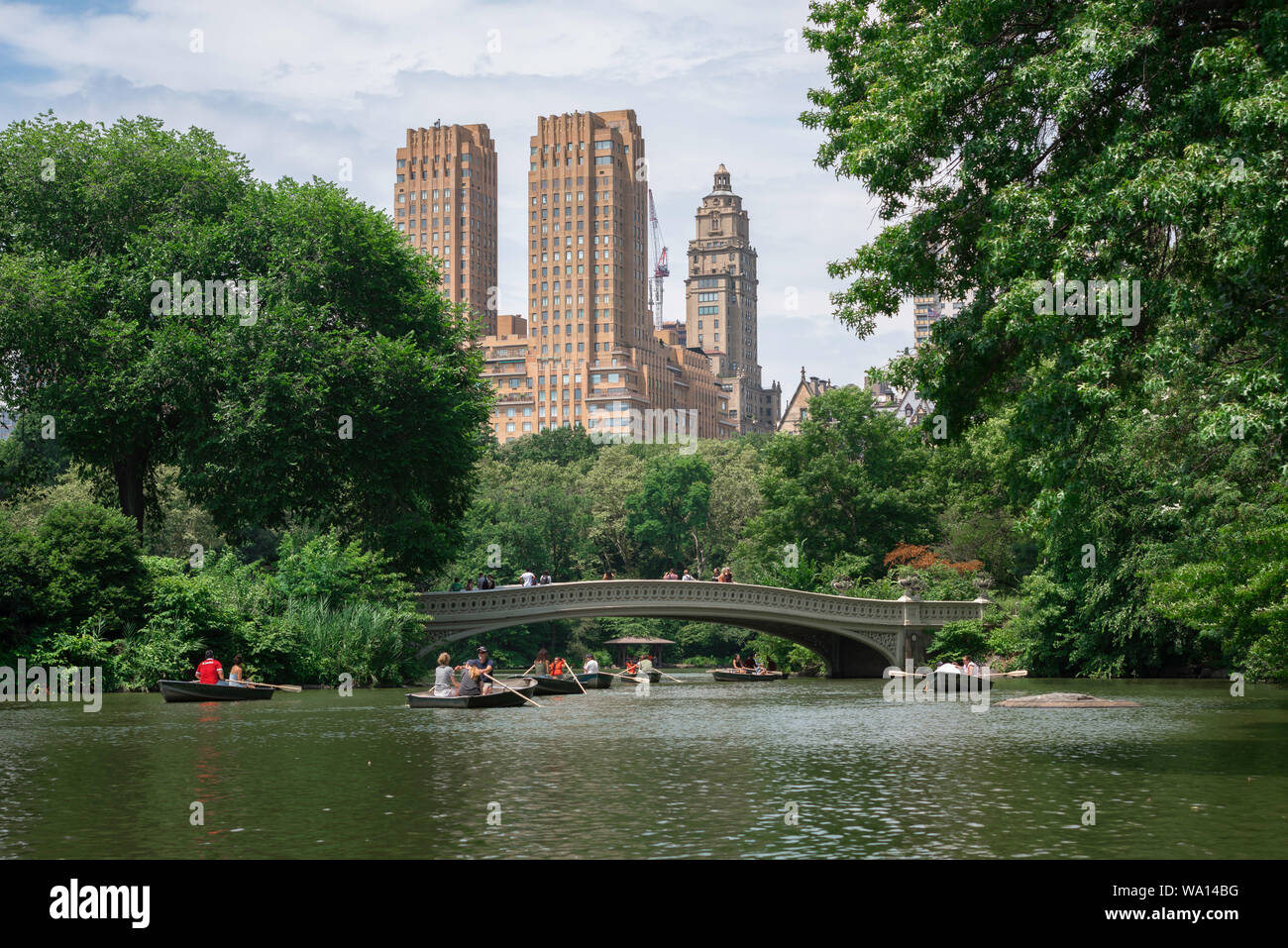 Il Central Park di New York, vista in estate di persone imbarcazioni a remi su Central Park Lake con il maestoso edificio di appartamenti in background, NYC, STATI UNITI D'AMERICA Foto Stock