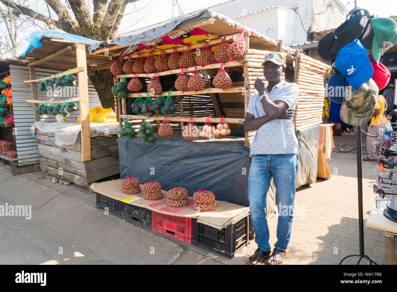 Nero uomo africano venditore ambulante si erge a frutta e verdura stallo che visualizza i dadi, pere di avocado, le cipolle di Graskop - Mpumalanga in Sudafrica Foto Stock