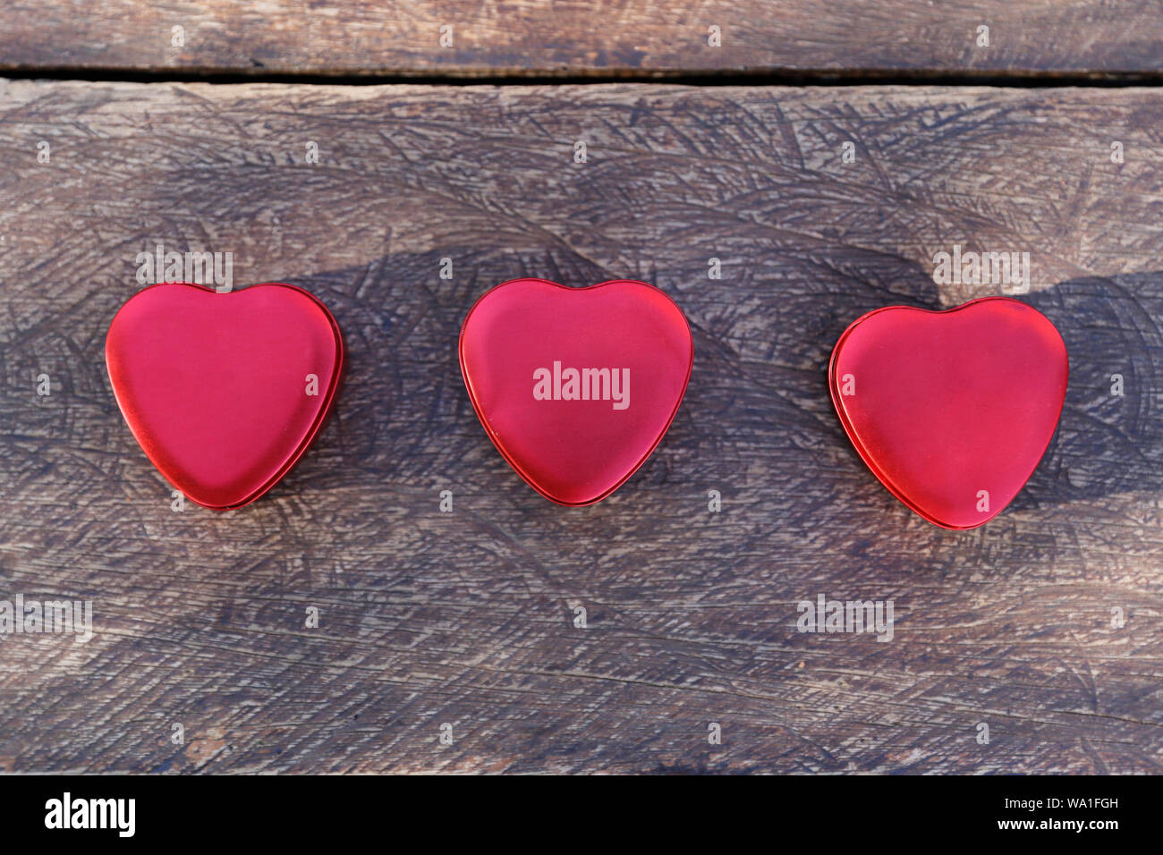 Tre rossi a forma di cuore di lattine di metallo, cuore, cuore di stagno su supporto in legno Foto Stock
