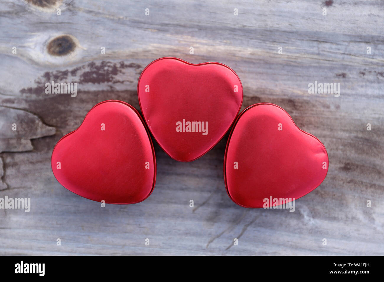 Tre rossi a forma di cuore di lattine di metallo, cuore, cuore di stagno su supporto in legno Foto Stock