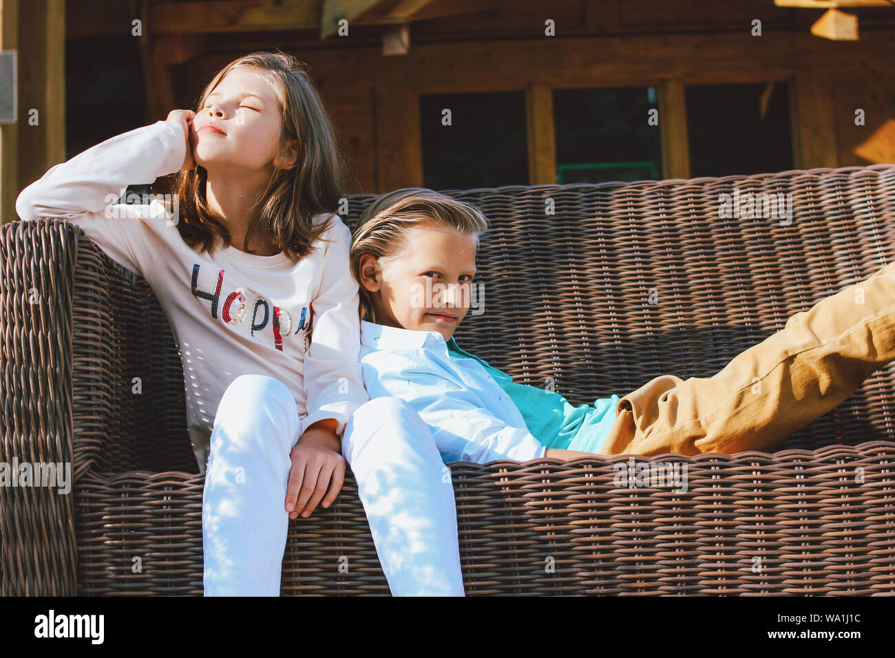 Attraente preteen bambini sorella e fratello, amici seduti sul divano in vimini nel cortile del cottage di legno Foto Stock