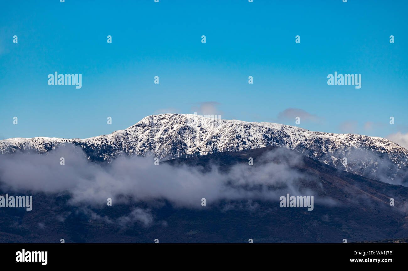 Montagna piena di alberi e le nuvole coprono le cime delle montagne innevate Foto Stock