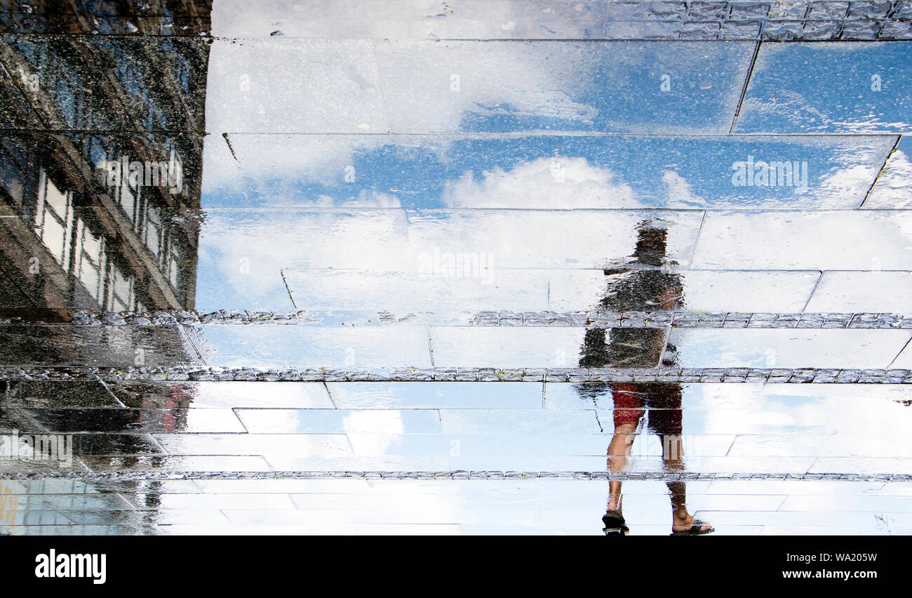 La riflessione ombra sagome di un giovane uomo che cammina su una strada bagnata su una soleggiata giornata d'estate in città Foto Stock