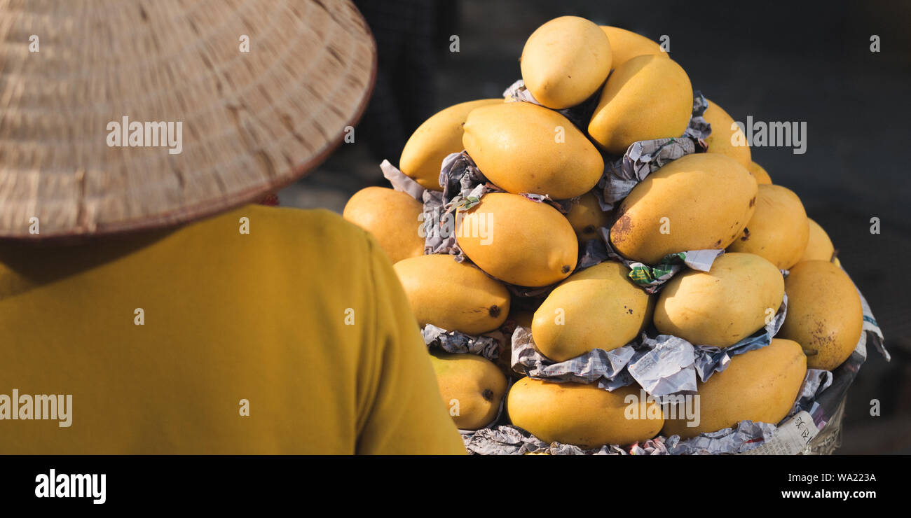 La città di Ho Chi Minh, Vietnam - Gennaio 9, 2019: un venditore ambulante in un cappello conico vende mango al mercato. Foto Stock