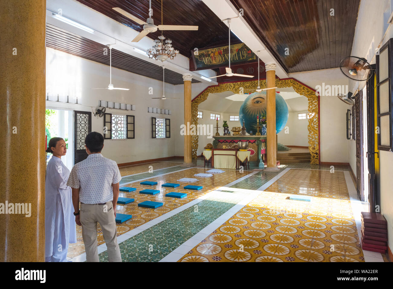 Tempio attendant (sinistra) & Unidentified uomo converse davanti della sfera d' occhio sinistro di Dio in Trung appeso Buu Toa Cao Dai, un Caodaist temple di Da Nang. Foto Stock