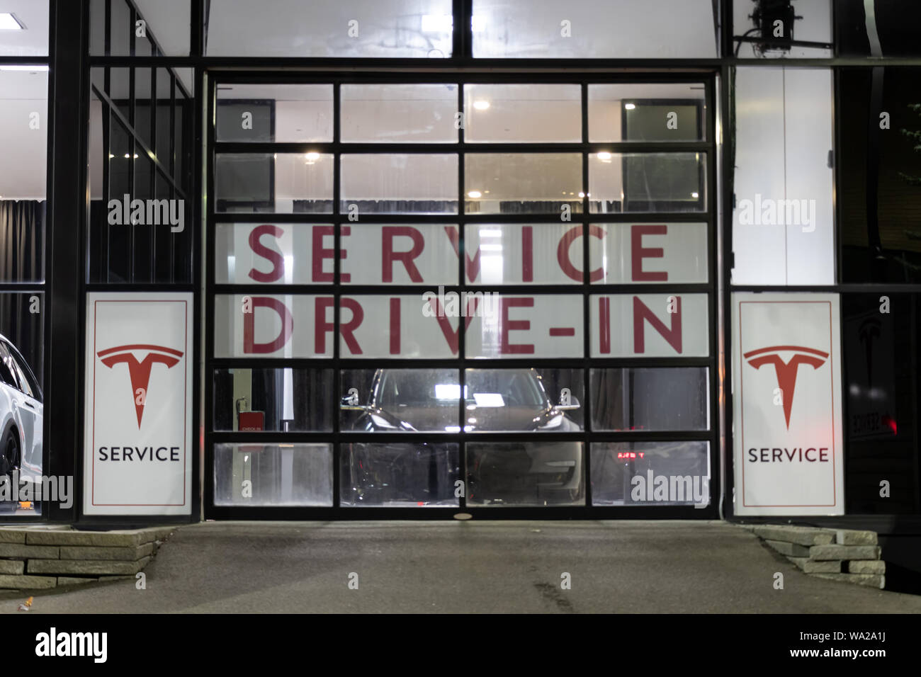 Ingresso della Tesla Service Center Drive-In di notte con Tesla Modello 3 dietro la porta. Foto Stock