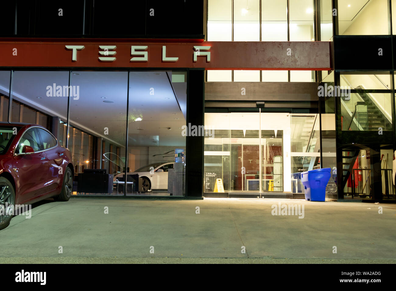Ingresso della Tesla Showroom visto di notte con un modello di Tesla 3 parcheggiate fuori e un altro sul display interno. Foto Stock