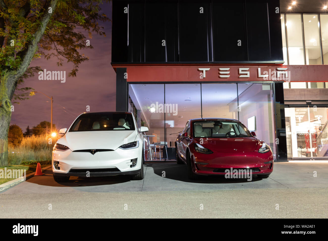 Tesla modello 3 e modello di Tesla X Parcheggiato fuori-parte anteriore della Tesla Showroom e centro di servizio su una chiara notte. Foto Stock