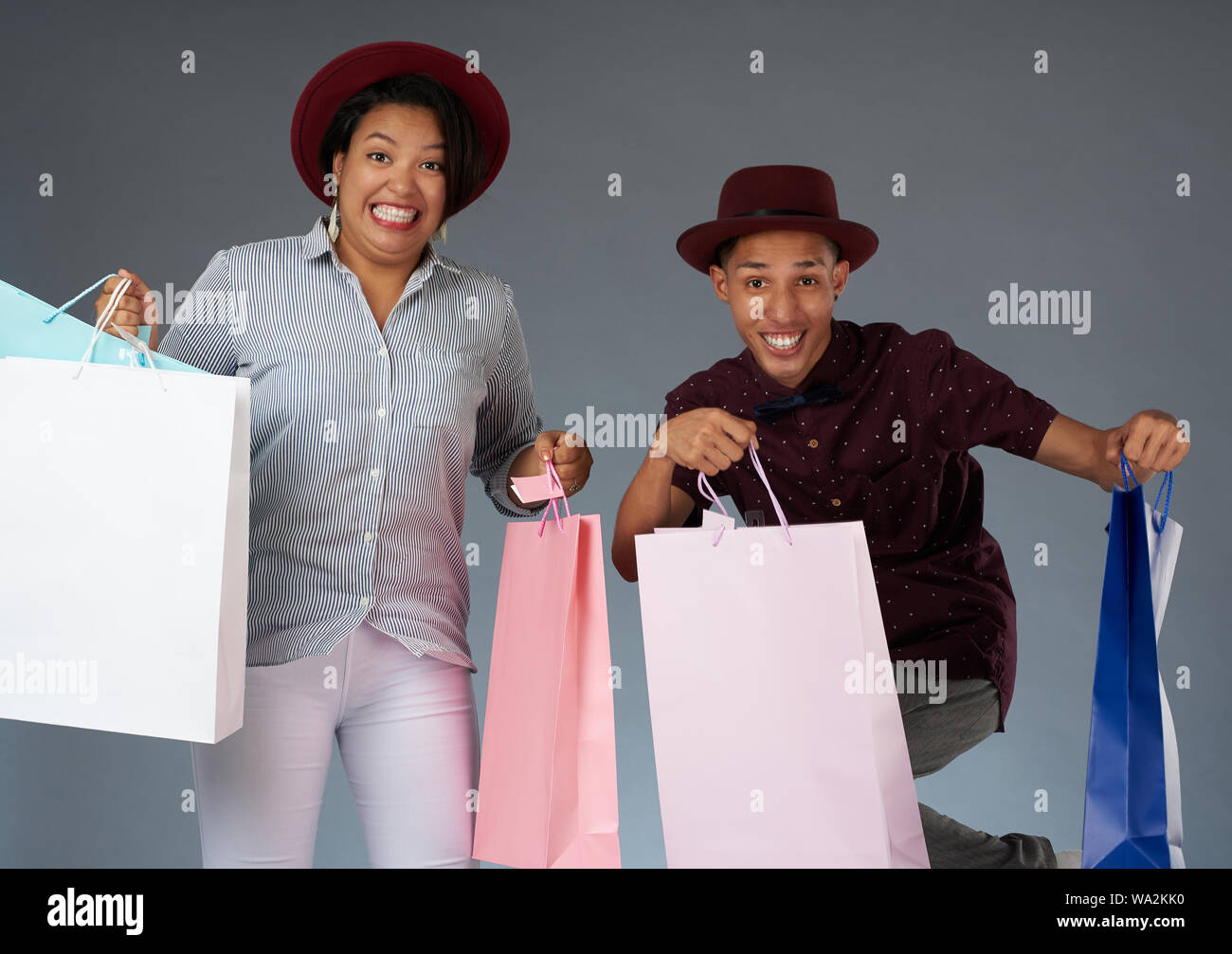 Sorridente jumping giovane coppia con shopping bags isolato su sfondo grigio Foto Stock