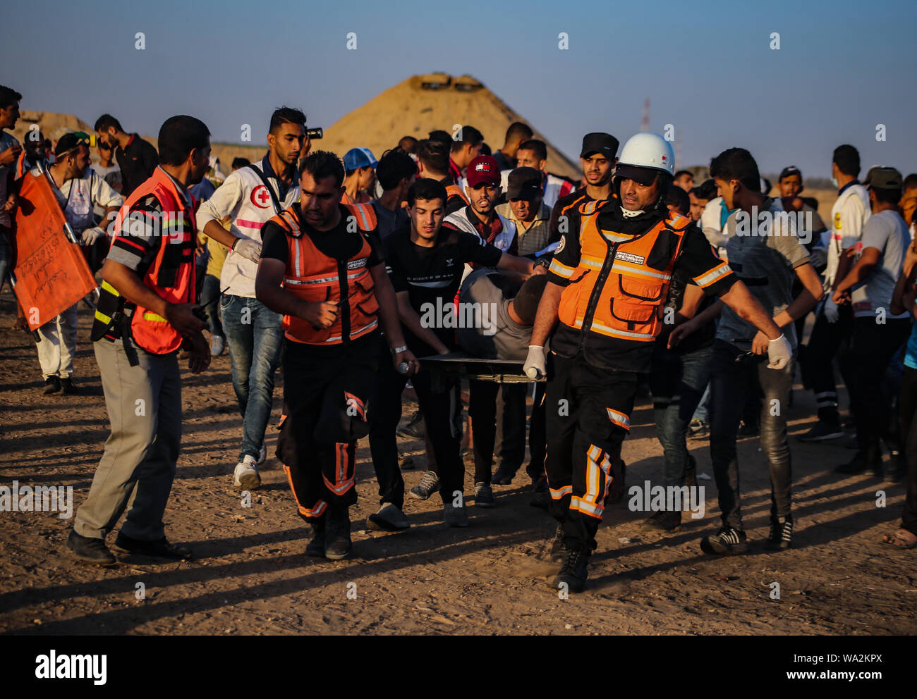 I medici portano un palestinese ferito durante gli scontri tra dimostranti palestinesi e israeliane attraverso la recinzione tra Gaza e Israele vicino a Khan Younis nel sud della striscia di Gaza pur dimostrando impegnativo il sollevamento dell'assedio imposto sulla cittadinanza per anni. Foto Stock