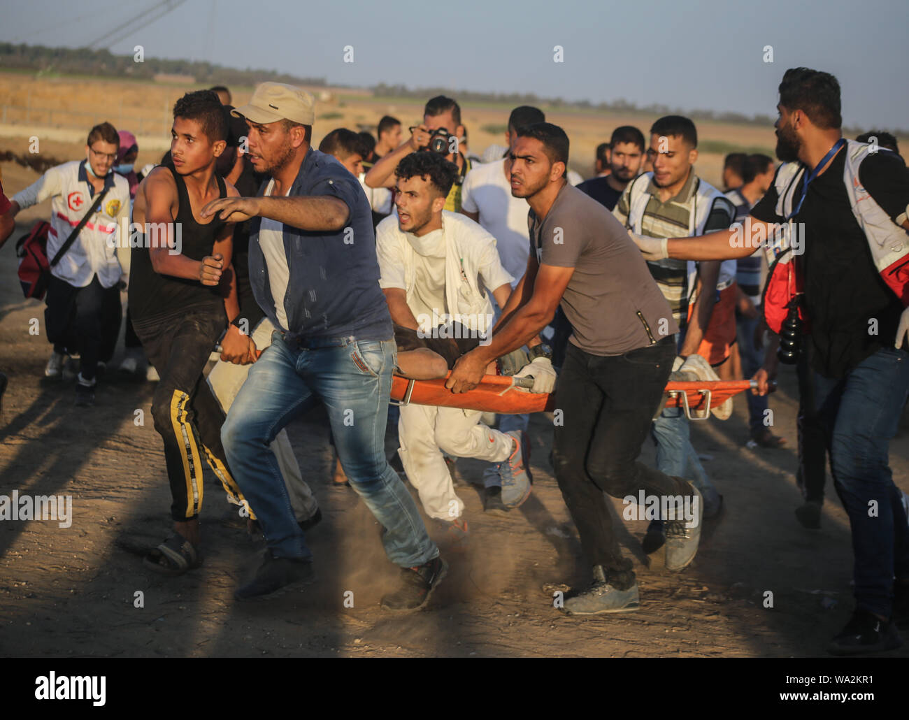 I medici portano un palestinese ferito durante gli scontri tra dimostranti palestinesi e israeliane attraverso la recinzione tra Gaza e Israele vicino a Khan Younis nel sud della striscia di Gaza pur dimostrando impegnativo il sollevamento dell'assedio imposto sulla cittadinanza per anni. Foto Stock