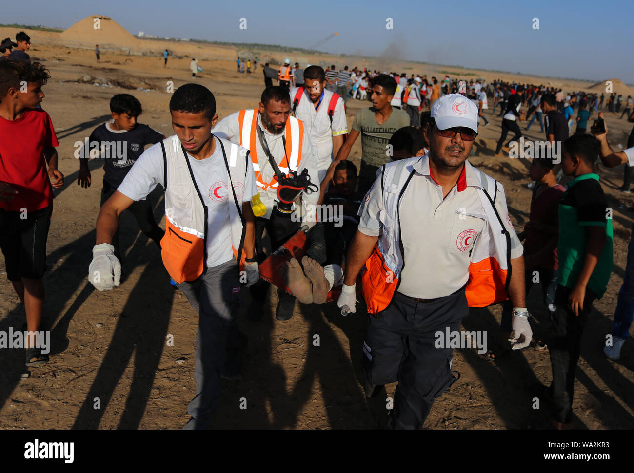 I medici portano un palestinese ferito durante gli scontri tra dimostranti palestinesi e israeliane attraverso la recinzione tra Gaza e Israele vicino a Khan Younis nel sud della striscia di Gaza pur dimostrando impegnativo il sollevamento dell'assedio imposto sulla cittadinanza per anni. Foto Stock