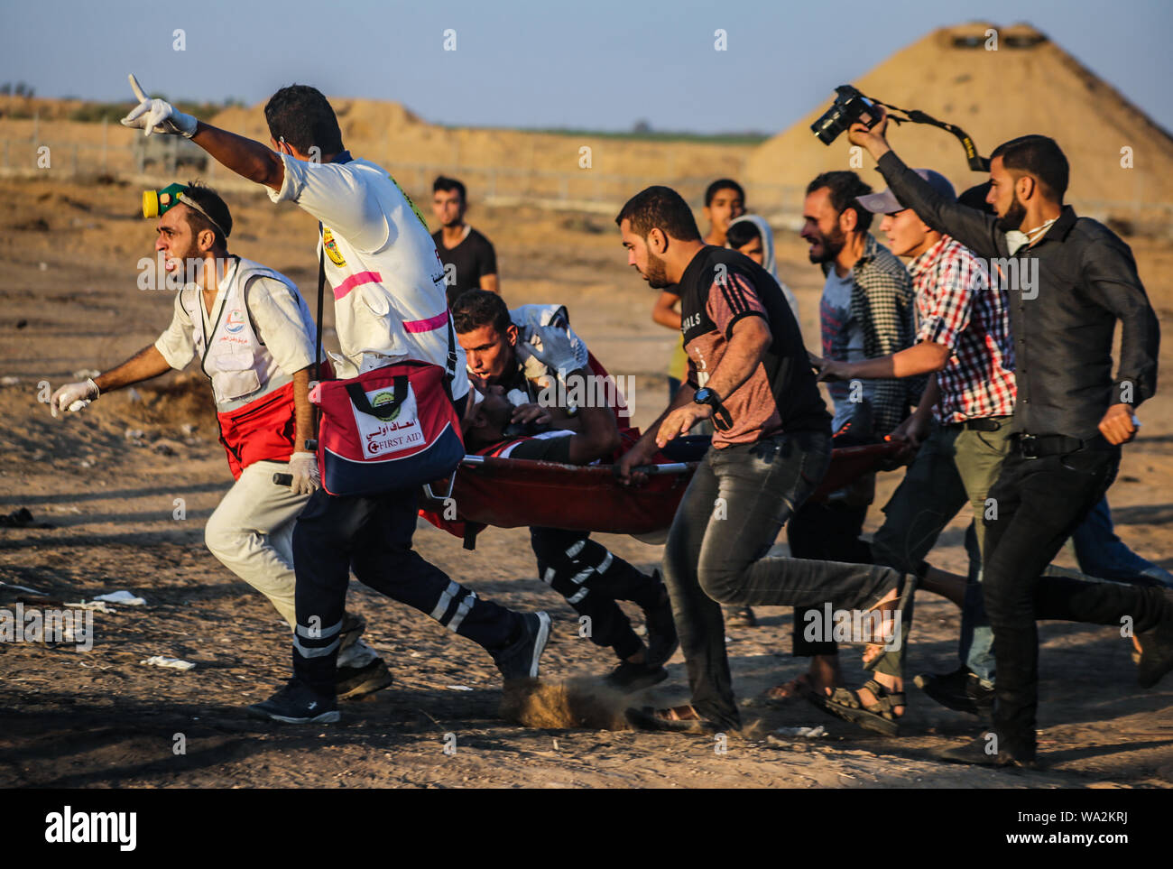 I medici portano un palestinese ferito durante gli scontri tra dimostranti palestinesi e israeliane attraverso la recinzione tra Gaza e Israele vicino a Khan Younis nel sud della striscia di Gaza pur dimostrando impegnativo il sollevamento dell'assedio imposto sulla cittadinanza per anni. Foto Stock