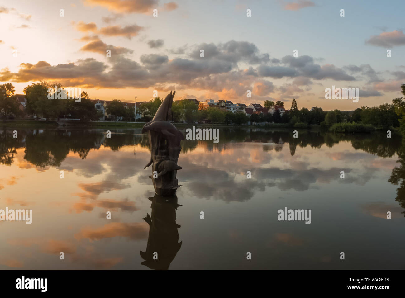 Un delfino scultura in un piccolo lago di un parco pubblico al di sotto di un nuvoloso cielo estivo Foto Stock