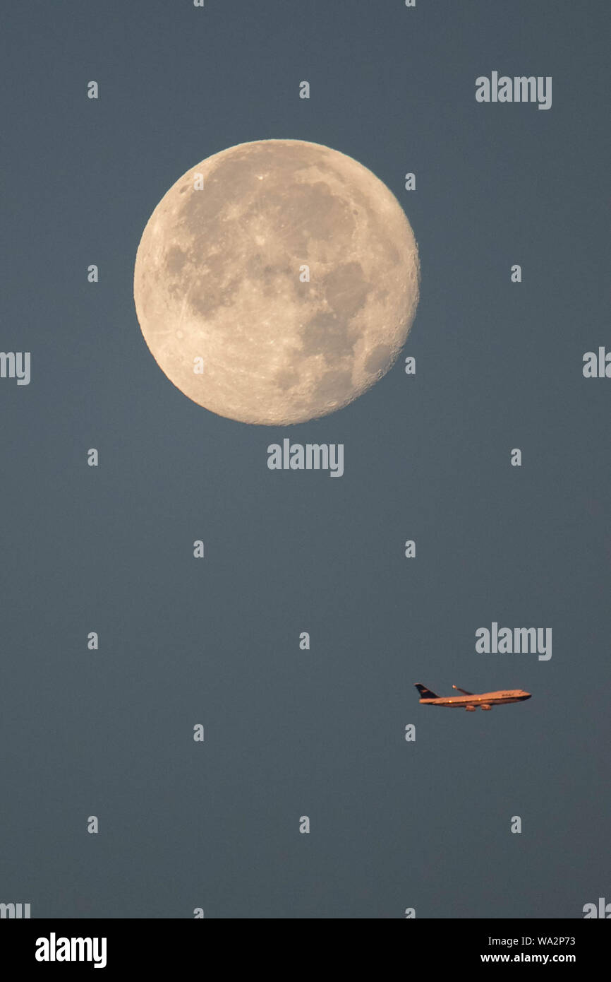 Londra REGNO UNITO. Il 17 agosto 2019. Un aeroplano vola sotto lo storione luna piena come sorge su Wimbledon southwest London​. La luna piena del mese di agosto è noto anche come lo storione Luna e il nome deriva dai nativi americani. Credito: amer ghazzal/Alamy Live News Foto Stock