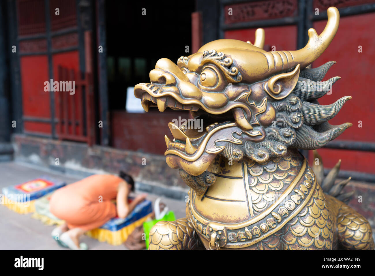 La testa di un Leone d'oro statua al monastero di Wenshu e sfocata donna cinese pregando inginocchiato in background in Chengdu Sichuan in Cina Foto Stock