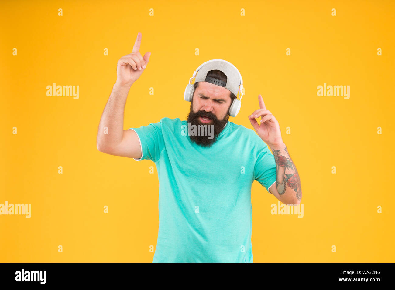 Nuova discoteca party hit. DJ uomo su sfondo giallo. Barba lunga guy godendo di sintonia a giocare a DJ party. Uomo Barbuto ascoltando la musica di cuffie per DJ. Hipster utilizzando un auricolare wireless per DJ discoteca. Foto Stock