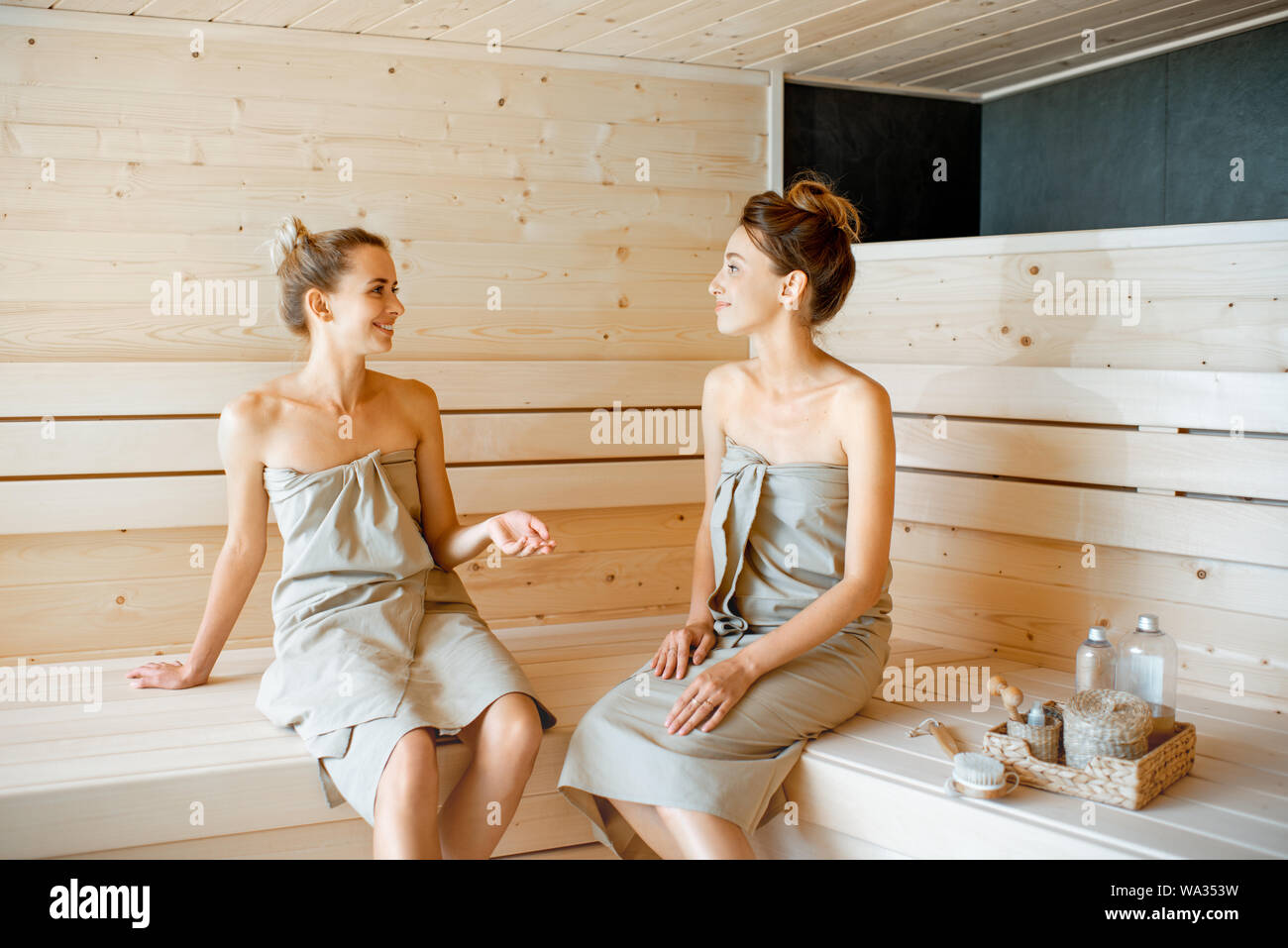 Due giovani fidanzate seduto e parlare insieme durante i momenti di relax nella sauna. Concetto di amicizia femminile e il trattamento termale Foto Stock