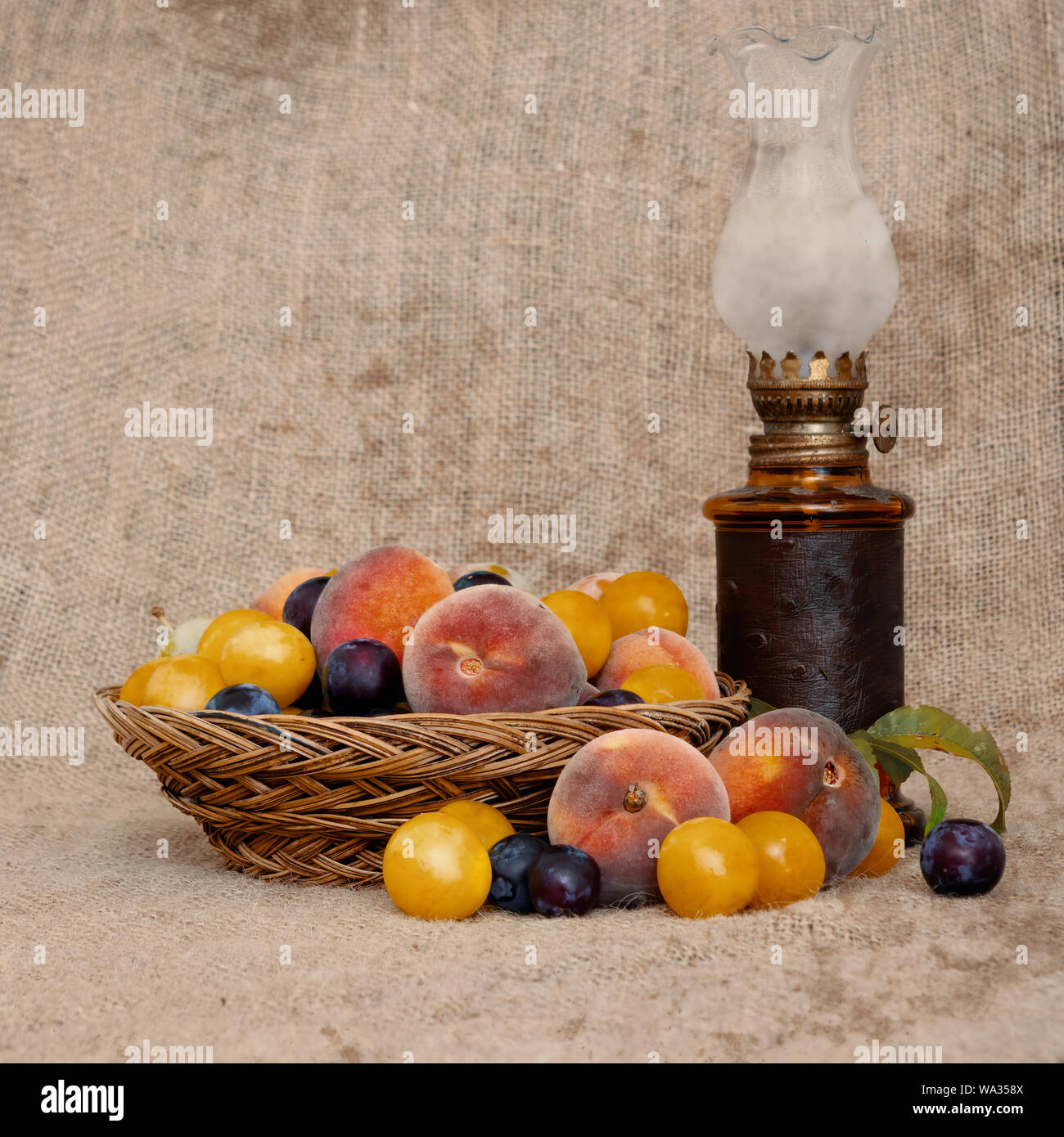 In vecchio stile heritage frutti da un lungo abbandonato frutteto di una vecchia ciotola di vimini, con l'annata olio lampada sopra tela di iuta. Ancora in vita. Foto Stock
