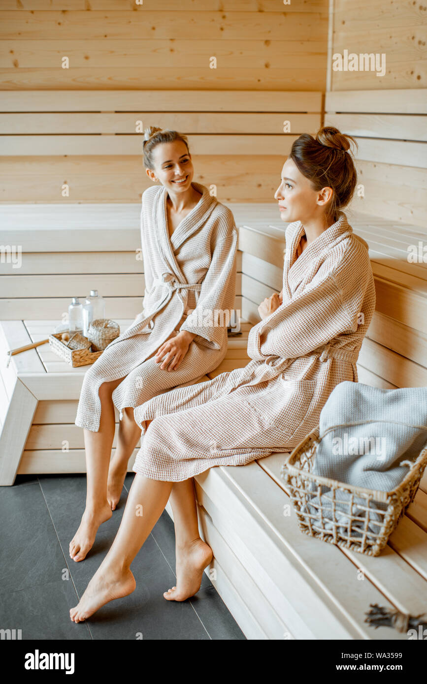 Due giovani belle ragazze in accappatoio seduti insieme durante i momenti di relax nella sauna di lusso Foto Stock