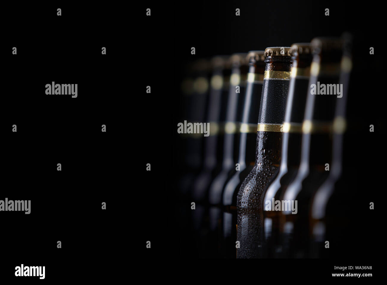 Le bottiglie di birra con etichette vuote schierate nella messa a fuoco selettiva su sfondo nero, uno con goccioline di brina Foto Stock