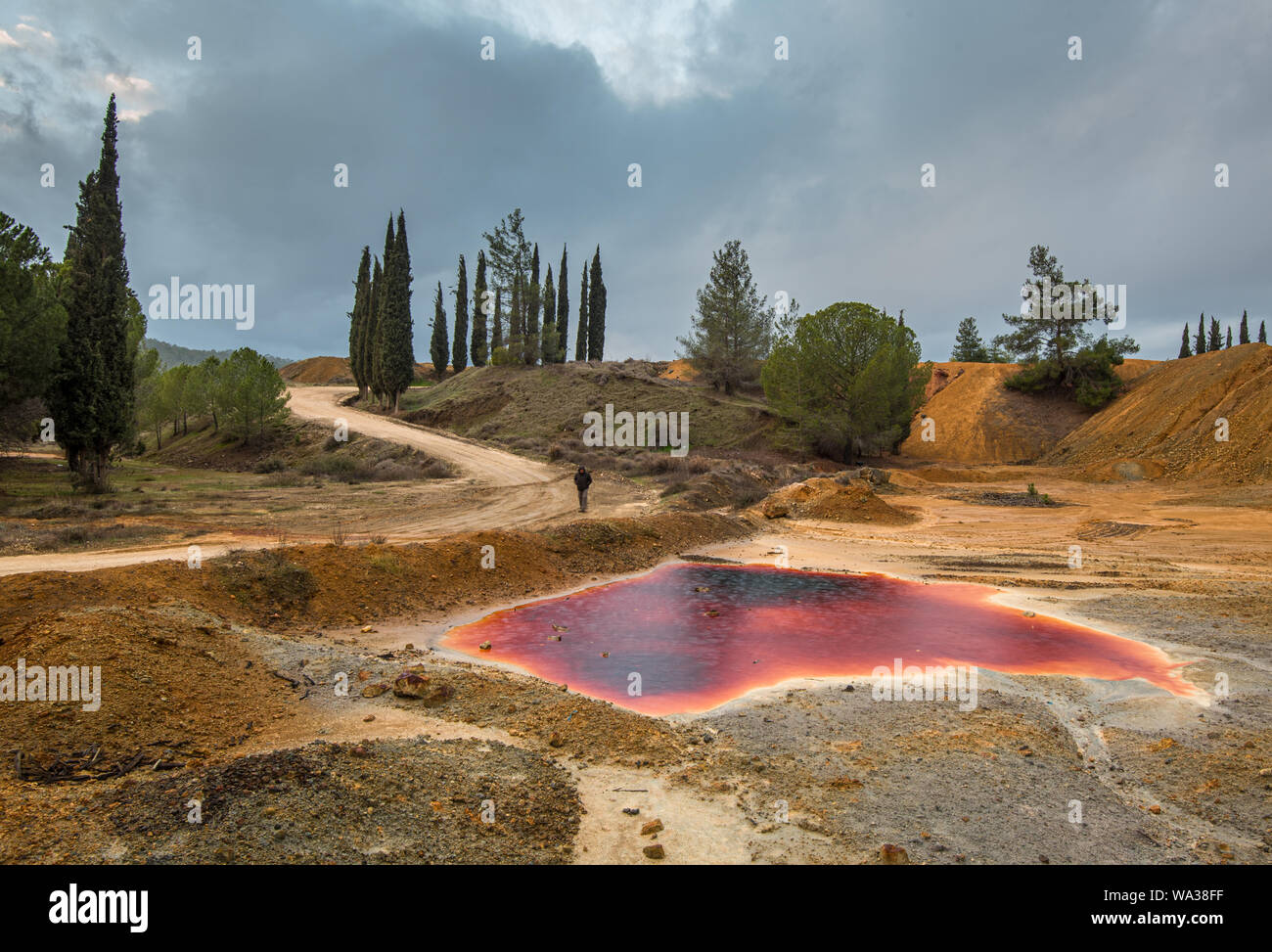 Irriconoscibile uomo a camminare in prossimità di un lago con red inquinato acque tossiche di una miniera di rame abbandonata a Mitsero area in Cipro Foto Stock