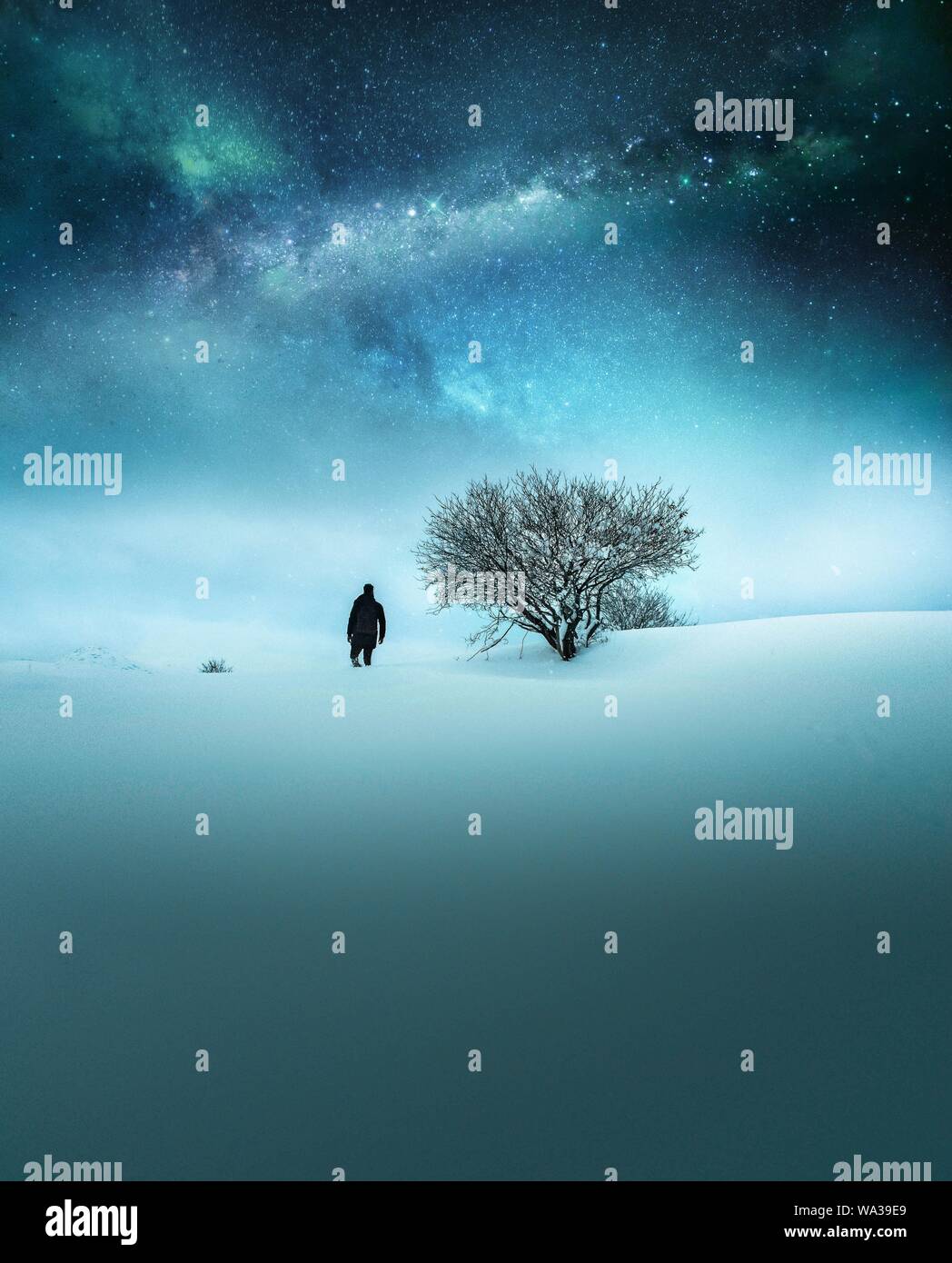 Concetto fantasy di un viaggiatore vestito in nero esplorando dentro la neve con cielo stellato mozzafiato Foto Stock