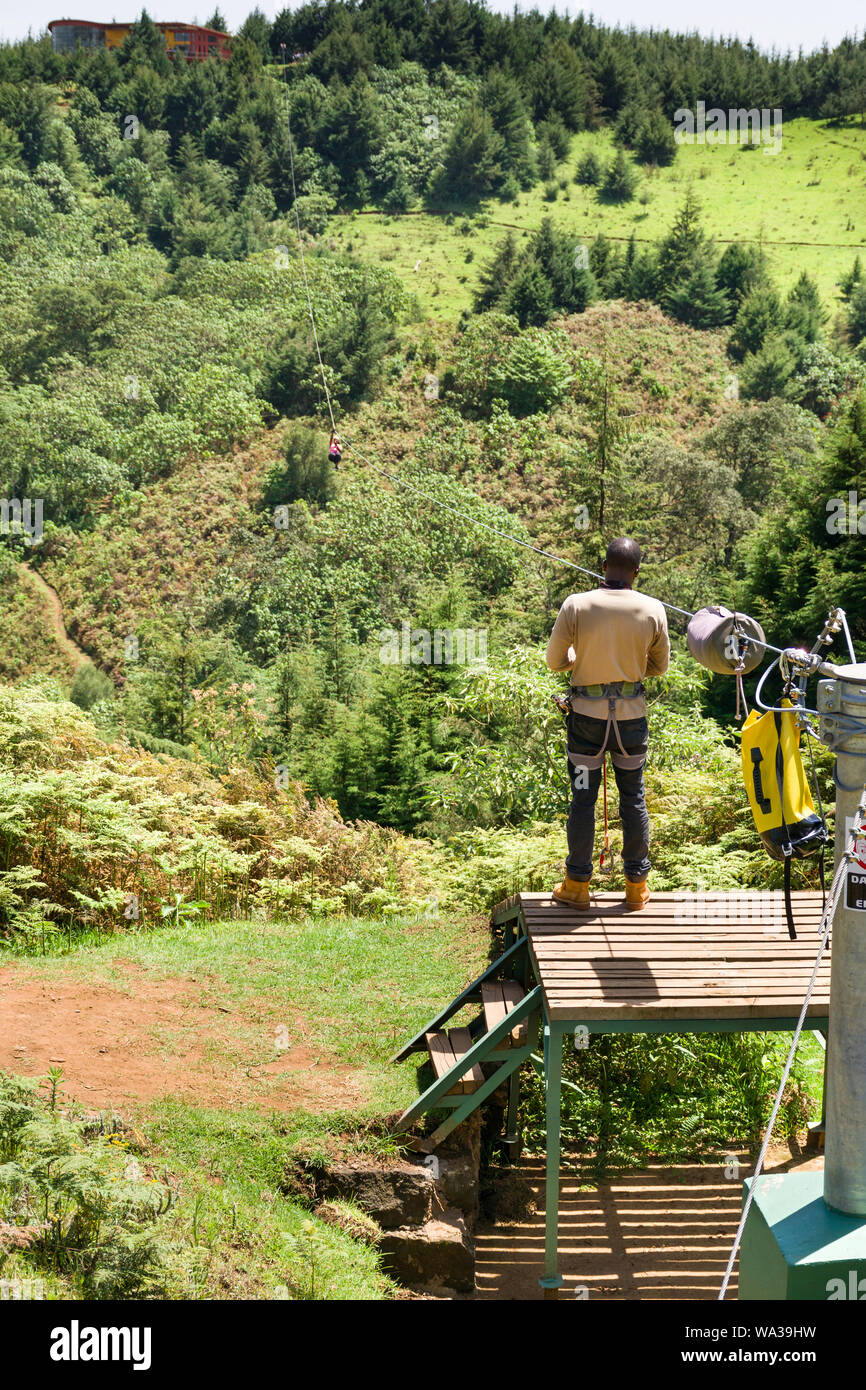 Una donna che viaggia su una linea di cerniera in corrispondenza della foresta il centro ricreativo con guida in attesa alla fine, Kenya Foto Stock