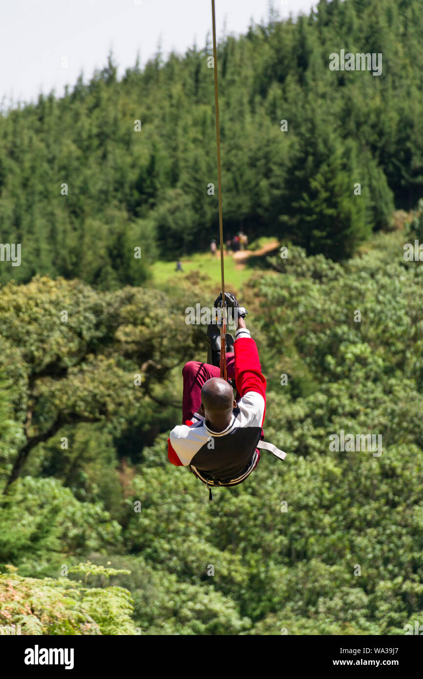 Un giovane uomo keniota che viaggiano su una linea di cerniera in corrispondenza della foresta il centro ricreativo, Kenya Foto Stock