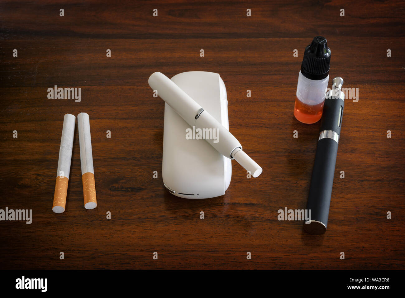 Fumo e impianti a vapore in confronto, normale sigaretta, riscaldatore del tabacco con bastoni e e-sigaretta con liquido su una tabella di colore marrone, spazio di copia selezionato, Foto Stock