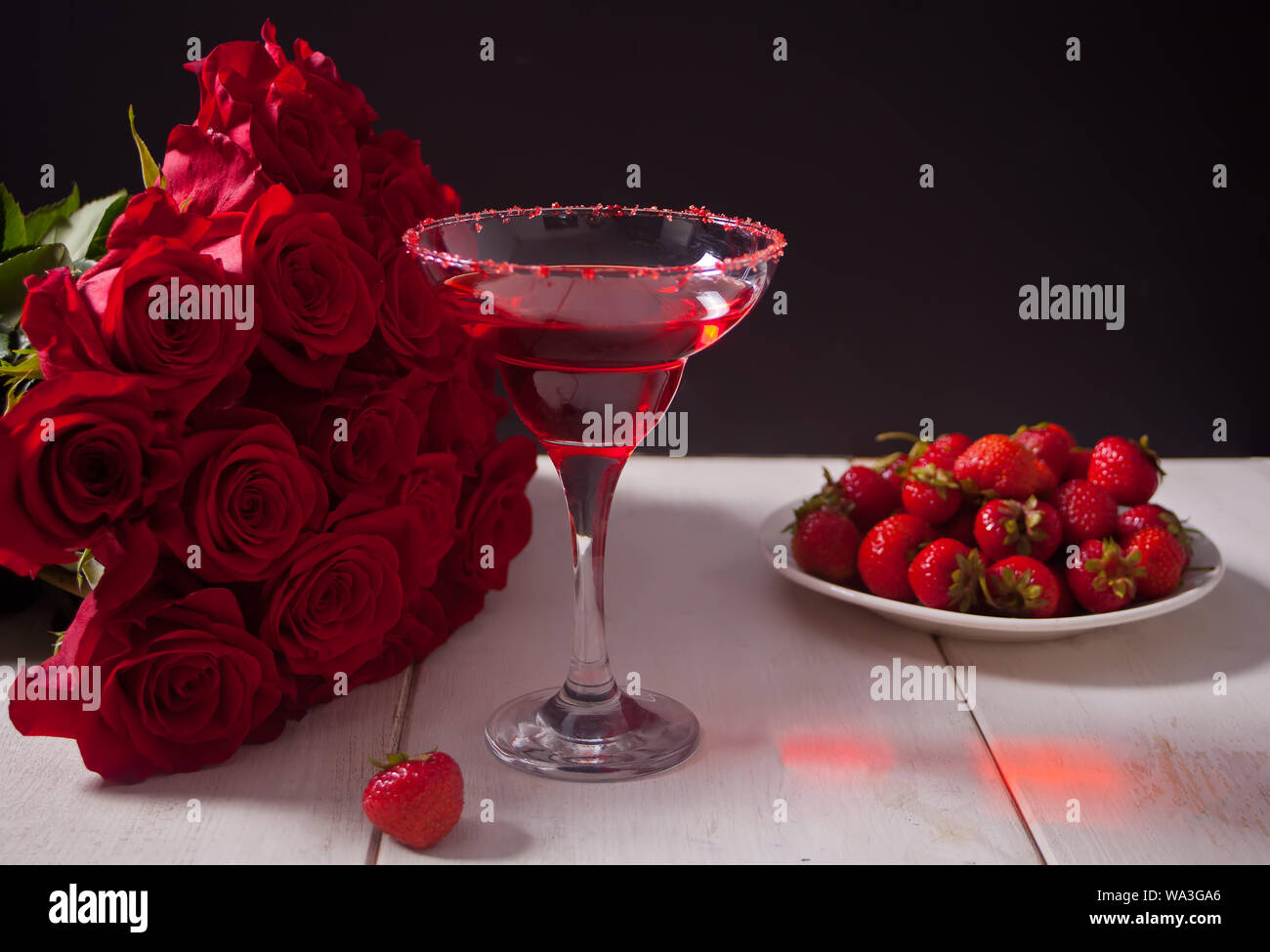 Rosso fresco esotici cocktail alcolico in vetro chiaro, piastra con bacche e rose rosse per cena romantica Foto Stock